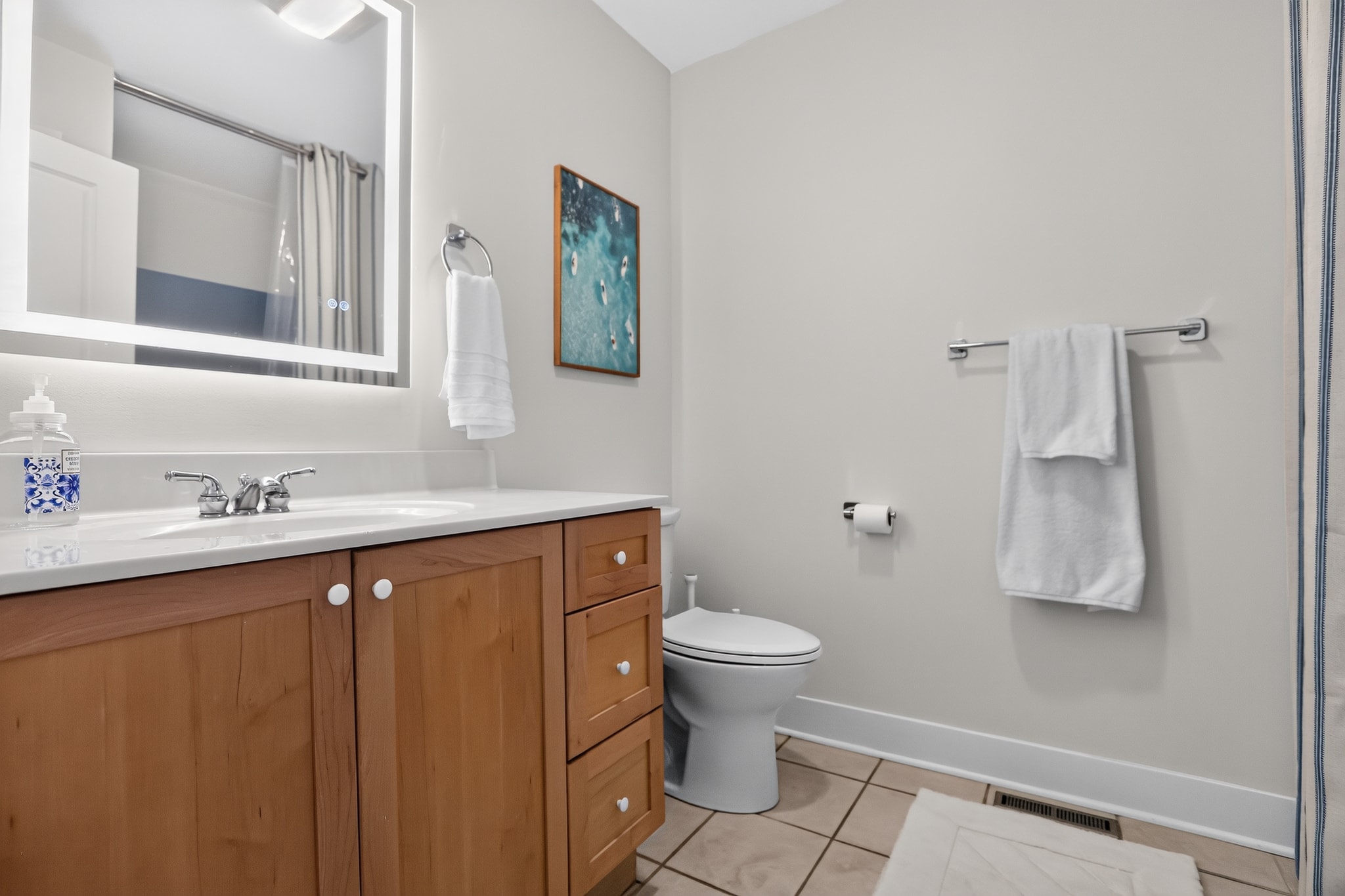 Bathroom with wood vanity, lighted mirror and coastal surf art